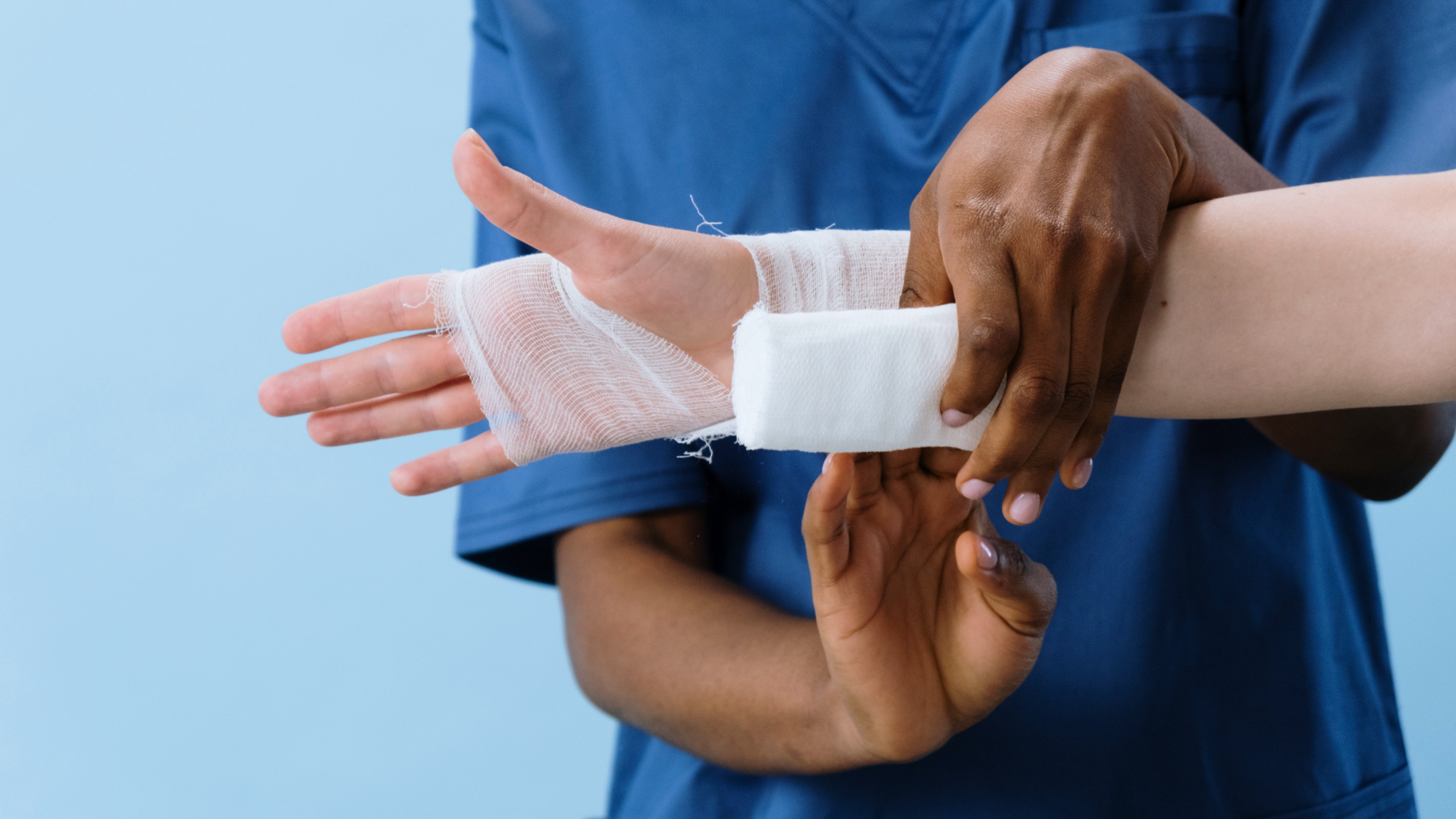 Zdjęcie przedstawia ręce dwóch osób. Jedna z tych osób bandażuje rękę tej drugiej.