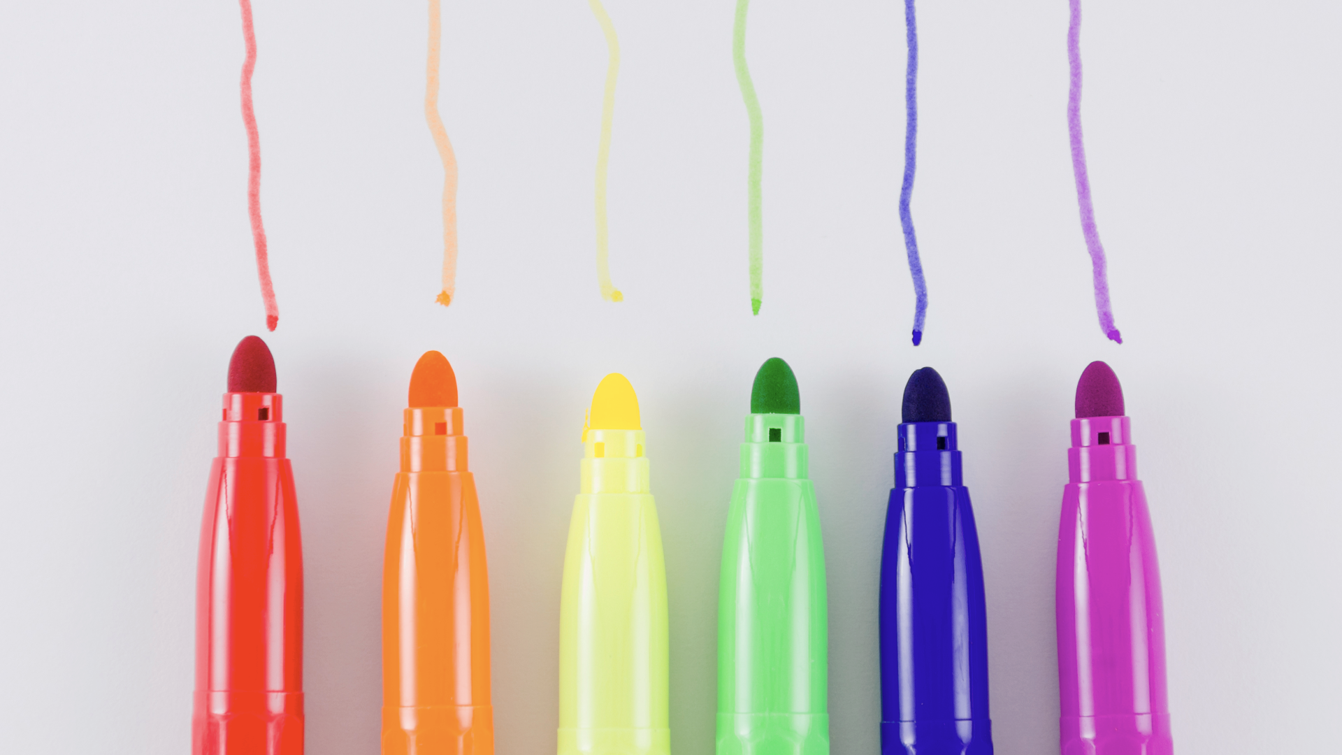 Zdjęcie przedstawia sześć flamastrów w różnych kolorach. Flamastry są równo ułożone. Przy każdym pisaku znajduje się kreska zrobiona flamastrem w danym kolorze.